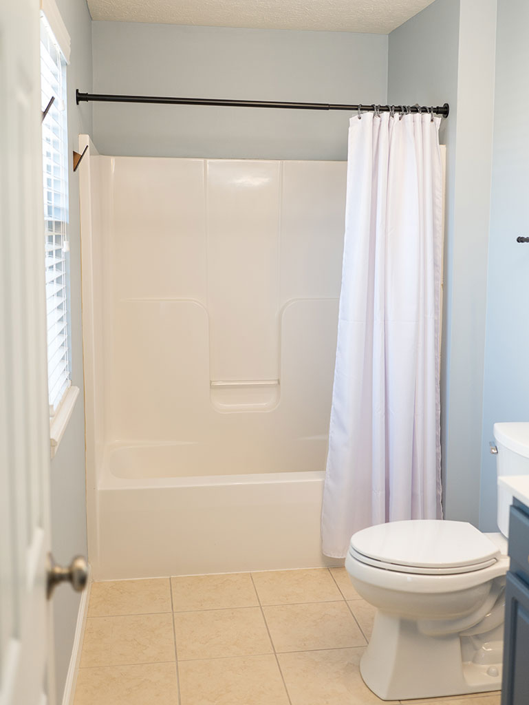 Small bathroom with a white bathtub and shower curtain, beige tile floor, and a toilet.